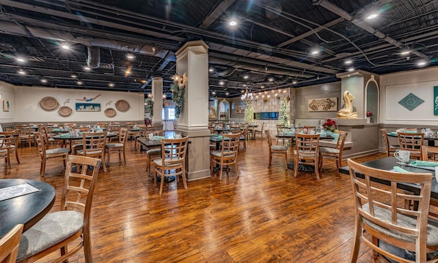 dining room featuring a bar, ornate columns, and wood finished floors