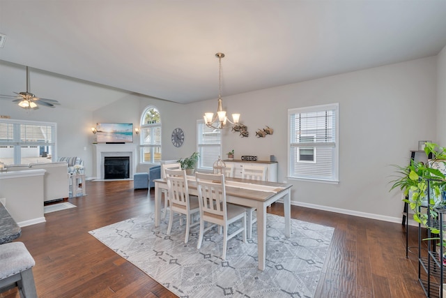 dining space with ceiling fan with notable chandelier, dark wood-type flooring, a fireplace, and a wealth of natural light