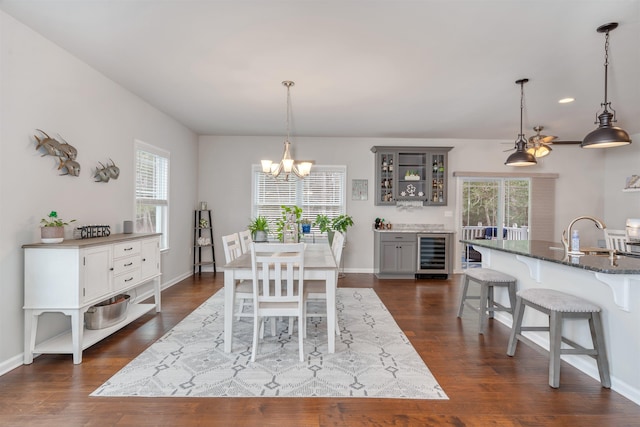 dining space with beverage cooler, a notable chandelier, dark wood finished floors, and baseboards