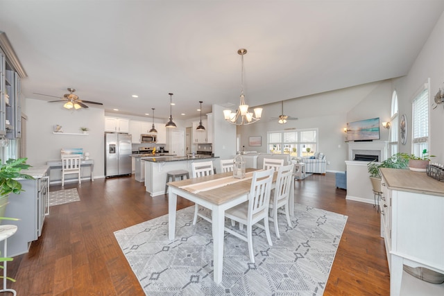 dining room featuring baseboards, dark wood-type flooring, a fireplace, and ceiling fan with notable chandelier