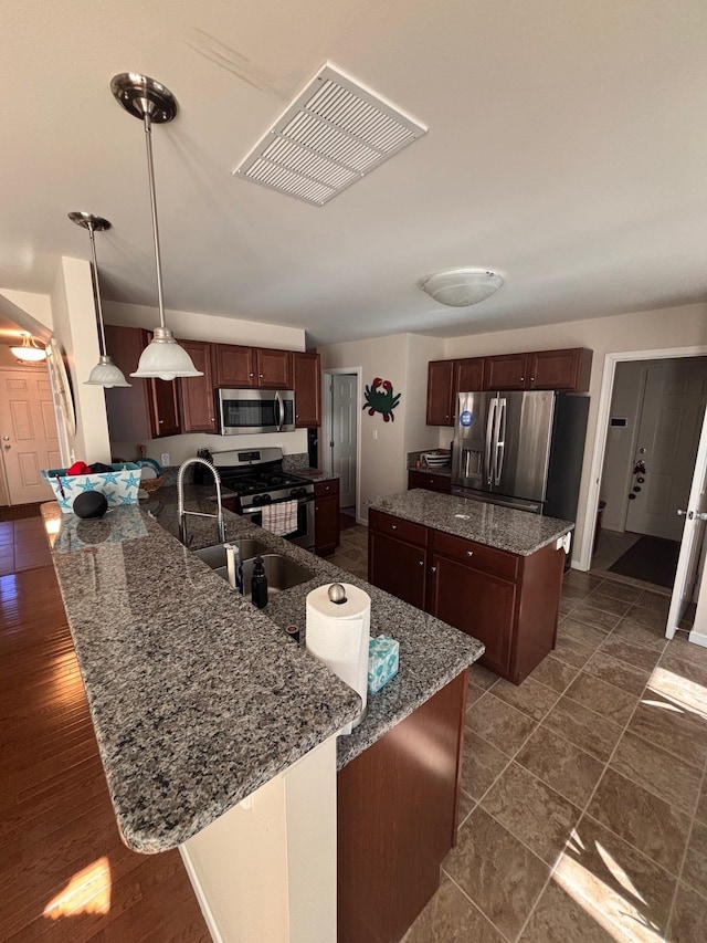 kitchen with stainless steel appliances, a peninsula, a sink, a kitchen island, and visible vents