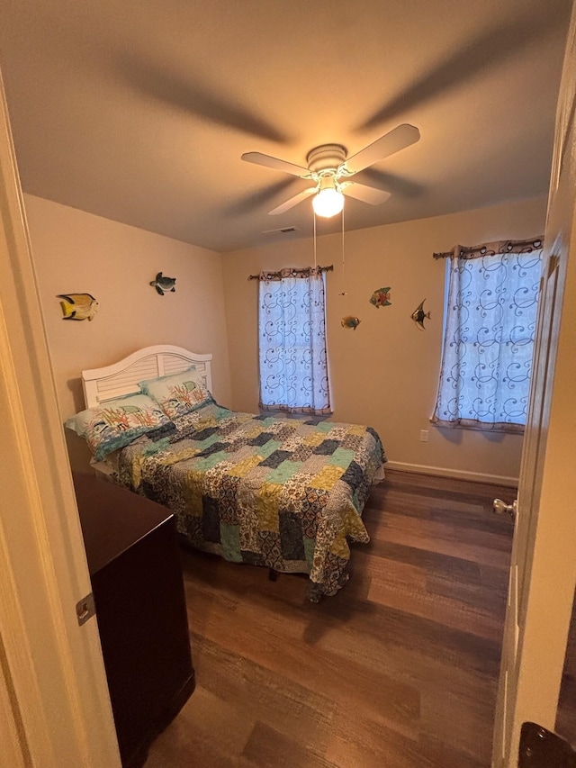 bedroom with a ceiling fan, visible vents, baseboards, and wood finished floors