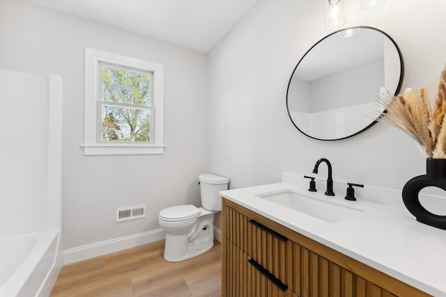 bathroom with wood finished floors, toilet, vanity, baseboards, and visible vents