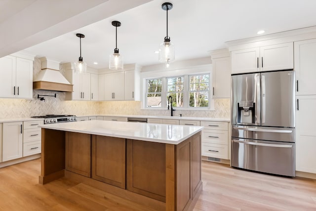 kitchen with a sink, stainless steel appliances, light wood-type flooring, custom exhaust hood, and white cabinets