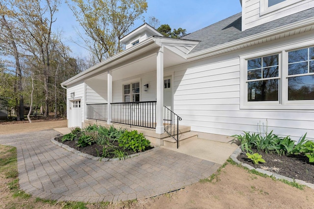 doorway to property with covered porch and a shingled roof