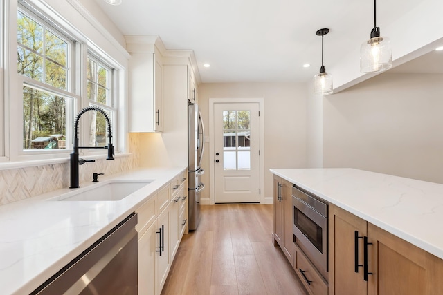kitchen featuring light stone counters, decorative backsplash, stainless steel appliances, light wood finished floors, and a sink