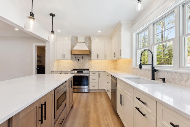 kitchen with light stone counters, stainless steel appliances, custom range hood, and a sink