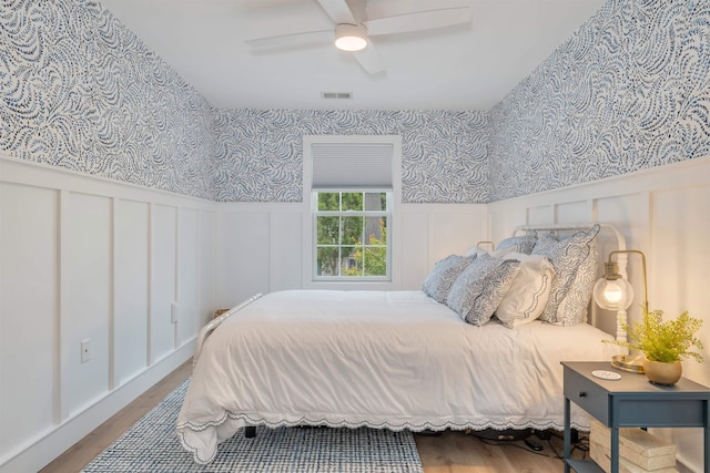202 Osprey Dr Unit 202, Cape May Court House, NJ 08210 - bedroom with a decorative wall, wood finished floors, wallpapered walls, a wainscoted wall, and a ceiling fan