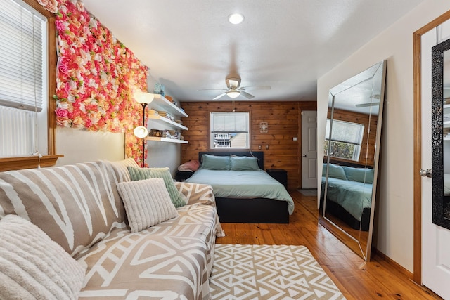 bedroom with light wood-type flooring, ceiling fan, and wood walls