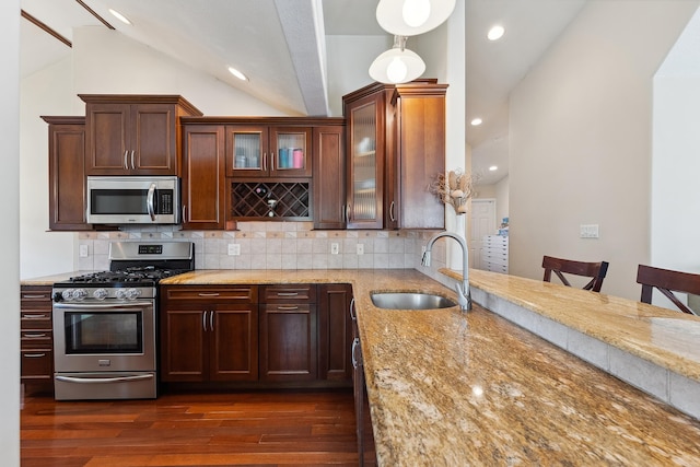 kitchen featuring light stone countertops, appliances with stainless steel finishes, vaulted ceiling, and sink