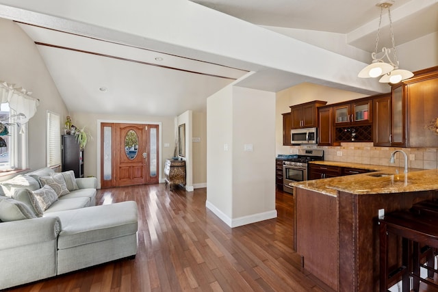 kitchen featuring backsplash, hanging light fixtures, appliances with stainless steel finishes, a kitchen bar, and kitchen peninsula