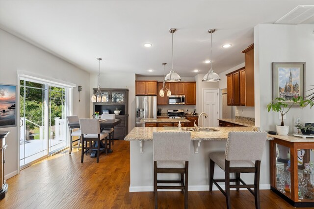 kitchen with pendant lighting, stainless steel appliances, sink, dark hardwood / wood-style floors, and light stone counters