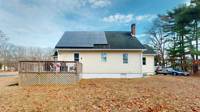 rear view of property featuring solar panels, a lawn, and a wooden deck