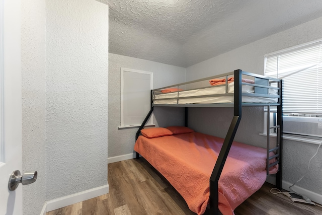 bedroom featuring wood-type flooring, cooling unit, and a textured ceiling