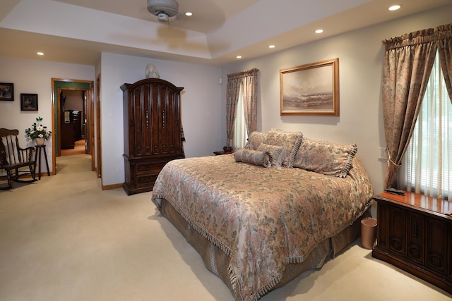 bedroom with a raised ceiling, light carpet, and ceiling fan