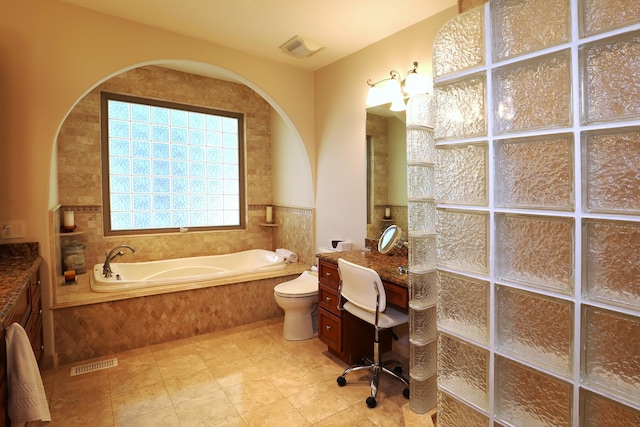 bathroom with tile patterned flooring, vanity, a relaxing tiled tub, and toilet