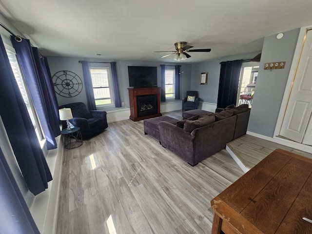 living room featuring baseboards, a ceiling fan, light wood-style flooring, and a fireplace