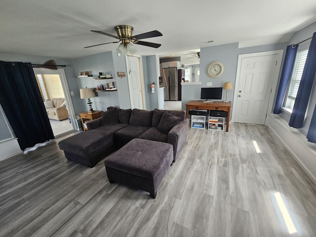living room with light wood-type flooring, a ceiling fan, and baseboards