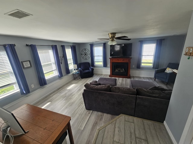 living room featuring visible vents, wood finished floors, a healthy amount of sunlight, a fireplace, and ceiling fan