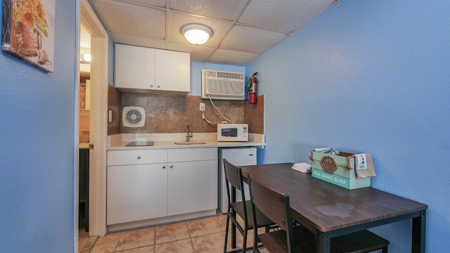 kitchen with white microwave, tasteful backsplash, a sink, white cabinets, and a paneled ceiling