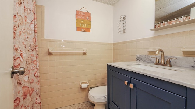 full bathroom with tile walls, toilet, wainscoting, tile patterned flooring, and vanity