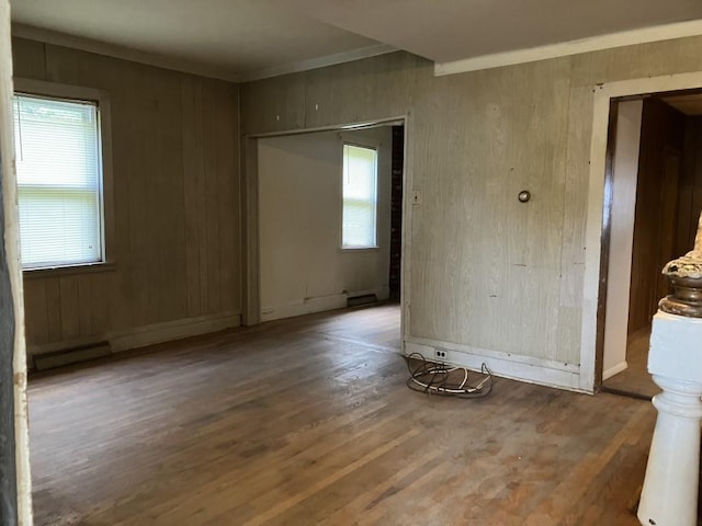 spare room featuring a baseboard heating unit, dark hardwood / wood-style flooring, crown molding, and wood walls