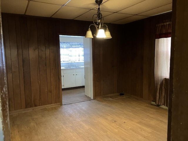 unfurnished room featuring a drop ceiling, light wood-type flooring, sink, and wooden walls