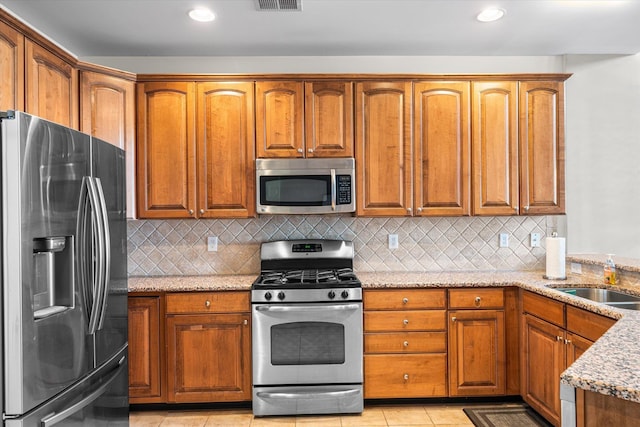 kitchen featuring light tile patterned flooring, sink, decorative backsplash, light stone counters, and stainless steel appliances