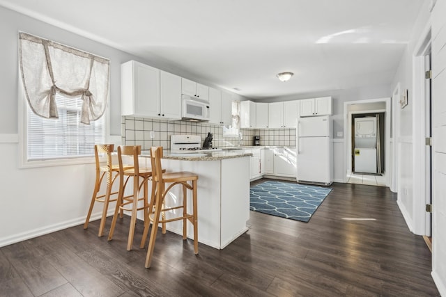 kitchen featuring white appliances, white cabinets, decorative backsplash, a kitchen bar, and kitchen peninsula