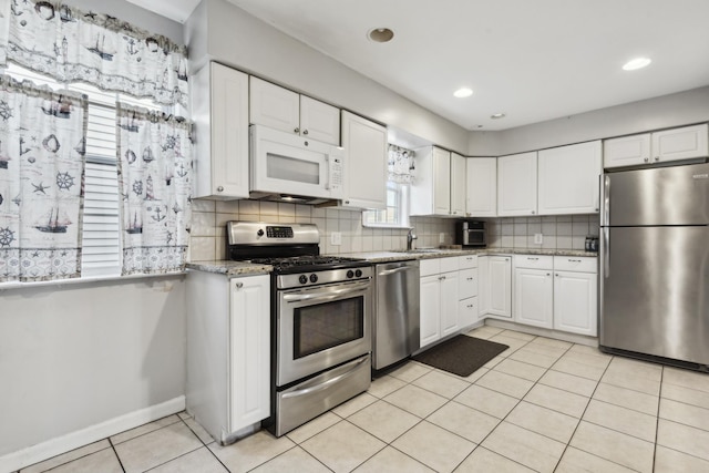 kitchen with light stone countertops, stainless steel appliances, sink, light tile patterned floors, and white cabinets