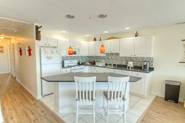 kitchen with a breakfast bar, white cabinets, decorative light fixtures, and white appliances