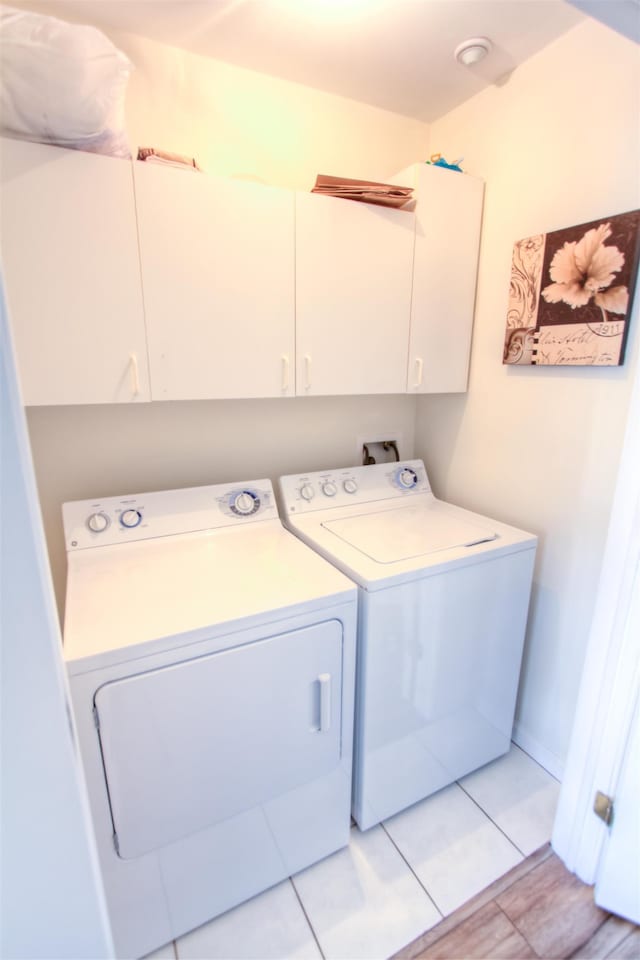 washroom featuring washing machine and clothes dryer, light tile patterned flooring, and cabinets