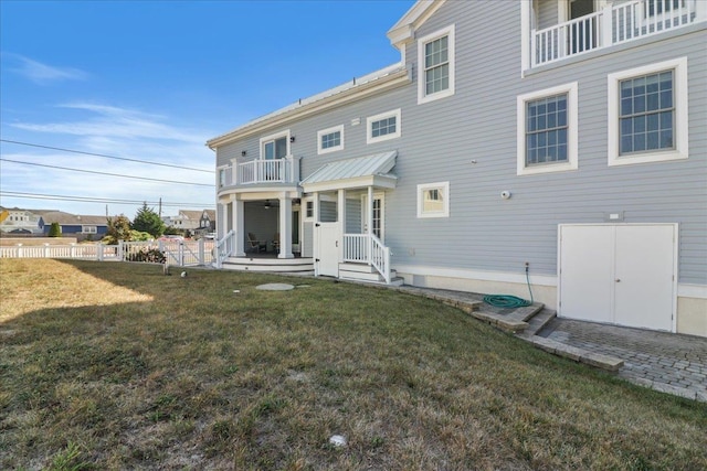 rear view of property featuring a lawn, fence, and a balcony