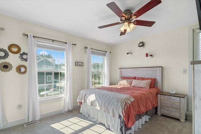 bedroom with light carpet, ceiling fan, visible vents, and baseboards