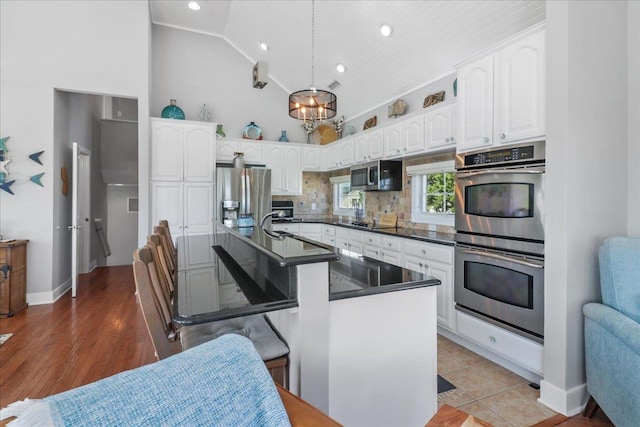 kitchen with stainless steel appliances, white cabinets, decorative backsplash, dark countertops, and decorative light fixtures