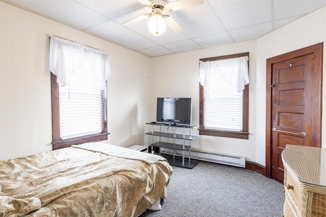 bedroom with carpet flooring, ceiling fan, a drop ceiling, a baseboard heating unit, and multiple windows