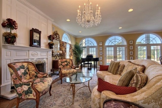 living area featuring crown molding, french doors, a high end fireplace, and an inviting chandelier