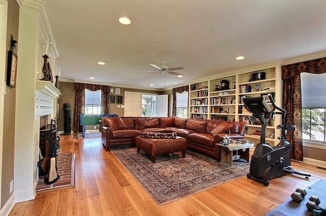 living room with ornamental molding, ceiling fan, built in features, a fireplace, and light hardwood / wood-style floors