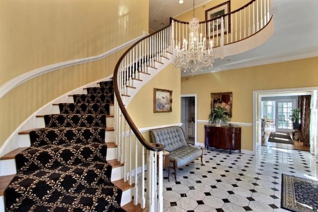 stairway with french doors, an inviting chandelier, crown molding, and a high ceiling