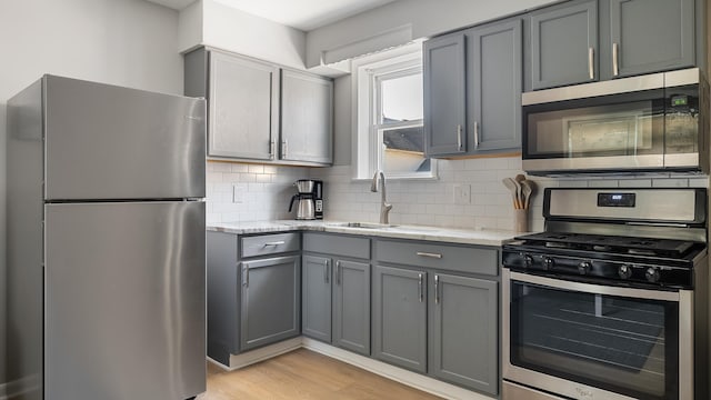 kitchen with appliances with stainless steel finishes, light stone counters, gray cabinetry, and sink