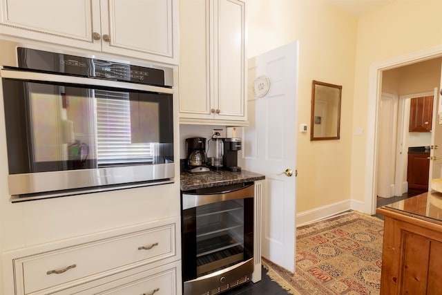 kitchen featuring dark stone counters, stainless steel oven, white cabinets, and beverage cooler