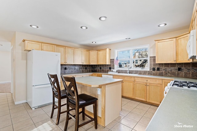 kitchen with sink, white appliances, a breakfast bar, a kitchen island, and light tile patterned flooring