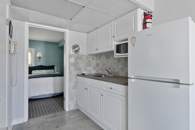 kitchen featuring freestanding refrigerator, a sink, dark countertops, light wood-style flooring, and white cabinets