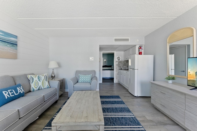living room featuring a textured ceiling, wood finished floors, and wooden walls