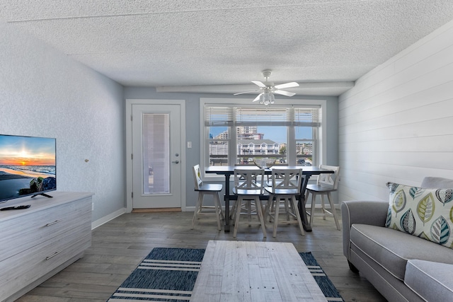 living area featuring a textured ceiling, wood finished floors, a ceiling fan, wood walls, and a textured wall