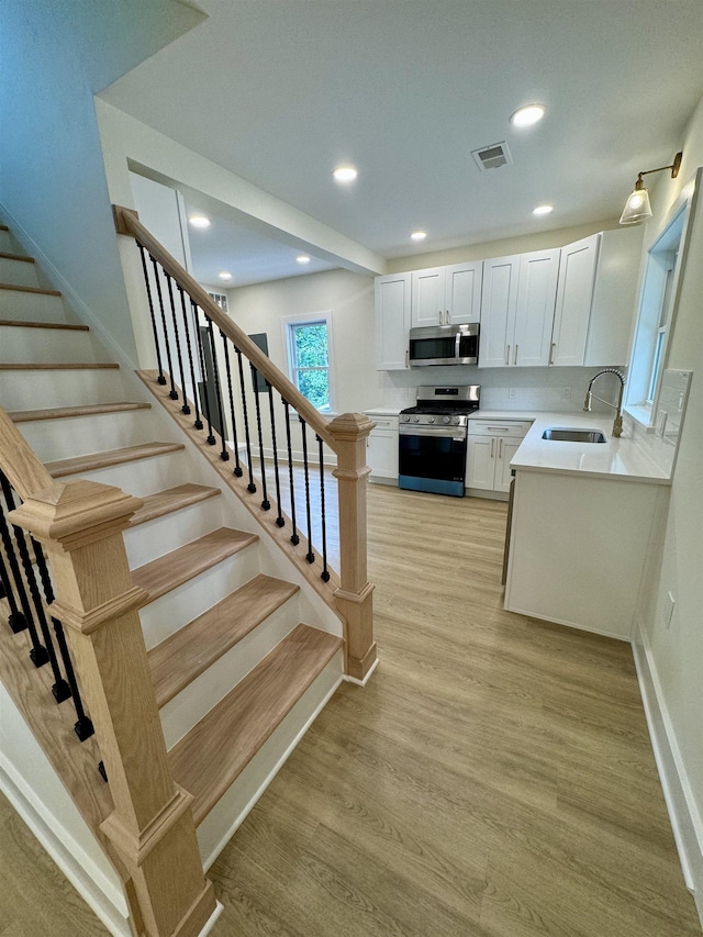 interior space with white cabinetry, sink, stainless steel appliances, and light wood-type flooring