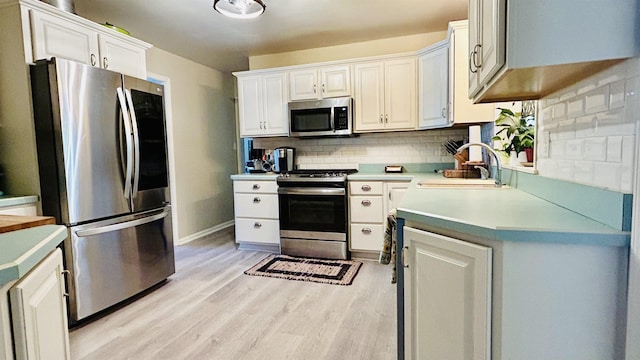 kitchen featuring white cabinetry, sink, light hardwood / wood-style flooring, decorative backsplash, and appliances with stainless steel finishes