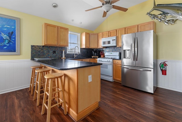 kitchen with sink, white appliances, dark wood-type flooring, a kitchen breakfast bar, and kitchen peninsula