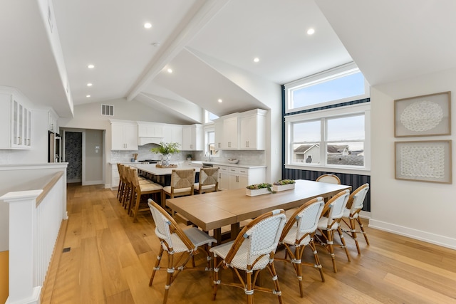 dining space featuring beam ceiling, light hardwood / wood-style flooring, and high vaulted ceiling