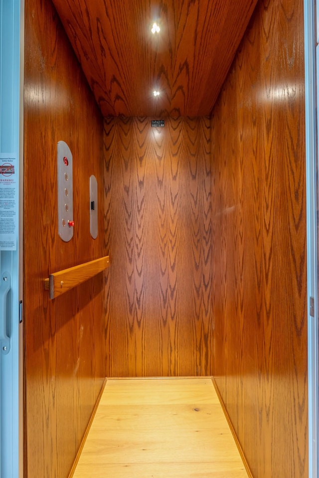 hall with elevator, wooden ceiling, and wooden walls